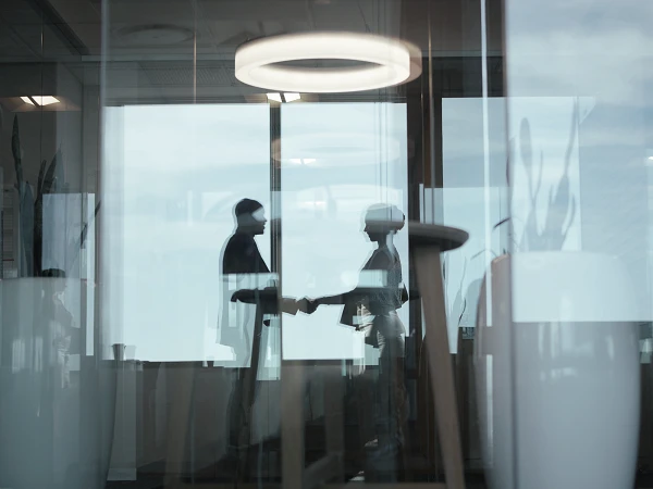 Händeschüttelnde Personen spiegeln sich in Scheibe eines modernen Büro