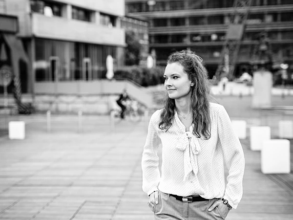 Frau mit lockigem Haar auf Promenade, Blick zur Seite, urbaner Hintergrund