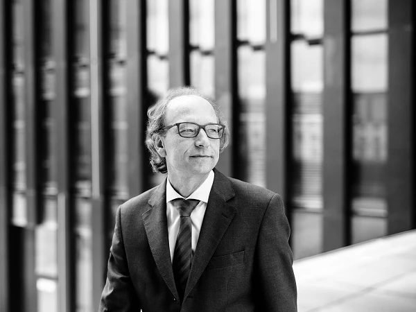 Mann mit Brille im Anzug vor moderner Glasfassade, Blick zur Seite