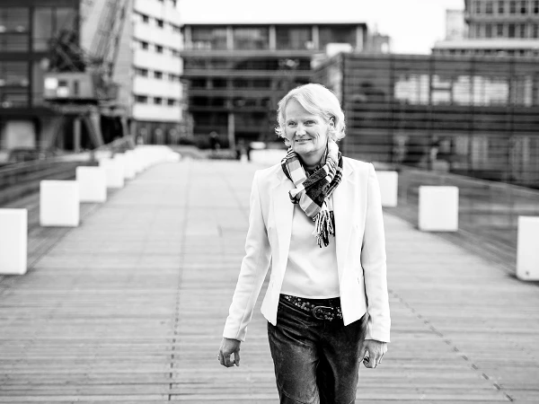 Frau im hellen Blazer mit Schal auf Holzsteg in urbaner Umgebung