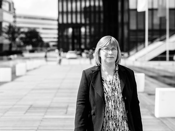 Frau mit Brille im Blazer, urbaner Hintergrund mit modernen Gebäuden