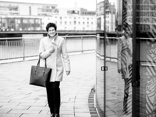 Frau mit heller Jacke und großer Tasche an Glasfassade mit Spiegelung
