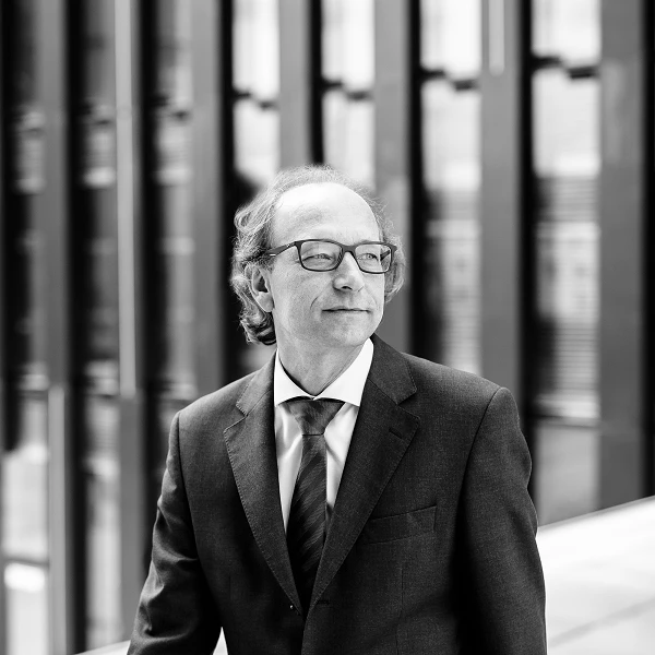 Man with glasses in suit, side glance in front of building facade
