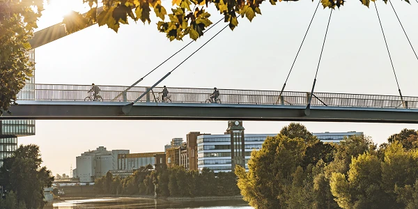 Pedestrian and bicycle bridge over river with cityscape in sunlight